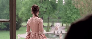 Movie still from “A Royal Affair” (2012), directed by Nikolaj Arcel – A woman in a pink dress standing in front of a fountain; Medium shot, Over the shoulder angle