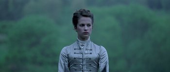 Movie still from “A Royal Affair” (2012), directed by Nikolaj Arcel – A young woman in a silver dress standing in front of a green background; Close Up shot, Low angle
