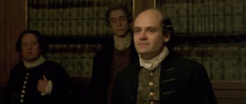 Movie still from “A Royal Affair” (2012), directed by Nikolaj Arcel – A man with a bald head standing next to another man; Medium shot, Over the shoulder angle