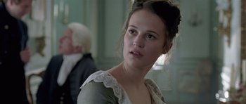 Movie still from “A Royal Affair” (2012), directed by Nikolaj Arcel – A young woman in a white dress looking to her left; Close Up shot, Over the shoulder angle