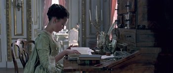 Movie still from “A Royal Affair” (2012), directed by Nikolaj Arcel – A woman sitting at a table reading a book; Medium shot, High angle