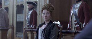 Movie still from “A Royal Affair” (2012), directed by Nikolaj Arcel – A woman sitting in a chair in front of a wall; Medium shot, Low angle