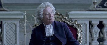 Movie still from “A Royal Affair” (2012), directed by Nikolaj Arcel – An old man in a wig sitting in a chair; Medium shot, High angle