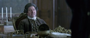 Movie still from “A Royal Affair” (2012), directed by Nikolaj Arcel – A man in a wig sitting in front of a table; Medium shot, Over the shoulder angle