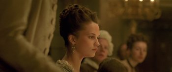 Movie still from “A Royal Affair” (2012), directed by Nikolaj Arcel – A beautiful young lady wearing a dress and earrings; Close Up shot, Over the shoulder angle