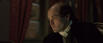 Movie still from “A Royal Affair” (2012), directed by Nikolaj Arcel – A man with a bald head wearing a black jacket; Close Up shot, Over the shoulder angle