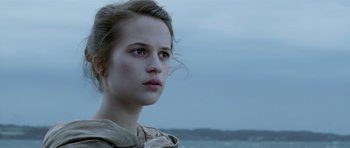 A young woman is looking into the distance while standing on the beach