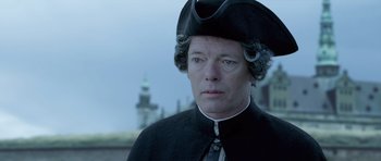 Movie still from “A Royal Affair” (2012), directed by Nikolaj Arcel – A man wearing a black hat and a black coat; Close Up shot, Over the shoulder angle
