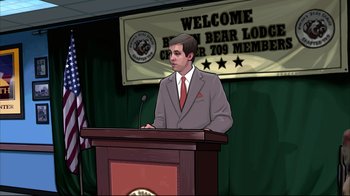 Movie still from “A Scanner Darkly” (2006), directed by Richard Linklater – A man standing at a podium in front of an american flag; Wide shot, Over the shoulder angle