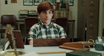 Movie still from “A Serious Man” (2009), directed by Joel Coen – A young man sitting at a table in front of an open book; Medium shot, Over the shoulder angle