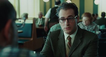 Movie still from “A Serious Man” (2009), directed by Joel Coen – A man in a suit and tie sitting at a table in front of other people; Close Up shot, Over the shoulder angle
