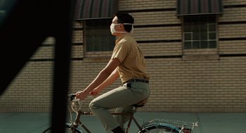 Movie still from “A Serious Man” (2009), directed by Joel Coen – A man riding a bicycle wearing a mask; Medium shot, Low angle