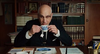 Movie still from “A Serious Man” (2009), directed by Joel Coen – An older man sitting at a table drinking from a cup; Medium shot, High angle