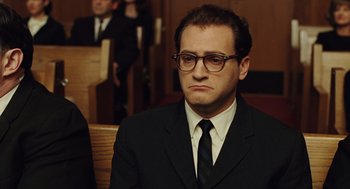 Movie still from “A Serious Man” (2009), directed by Joel Coen – A man in a suit and tie sitting in front of a crowd; Close Up shot, Low angle