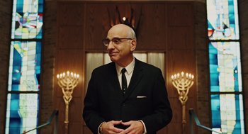 Movie still from “A Serious Man” (2009), directed by Joel Coen – A man in a suit and tie standing in front of candles in a room; Medium shot, Low angle