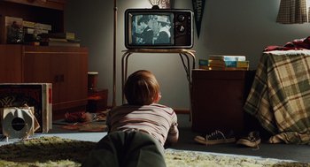 Movie still from “A Serious Man” (2009), directed by Joel Coen – A young boy is watching television in a living room; Wide shot, High angle