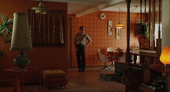 Movie still from “A Serious Man” (2009), directed by Joel Coen – A man standing in a living room next to a table; Wide shot, High angle