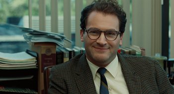 Movie still from “A Serious Man” (2009), directed by Joel Coen – A man in a suit and tie smiling for the camera; Close Up shot, Over the shoulder angle