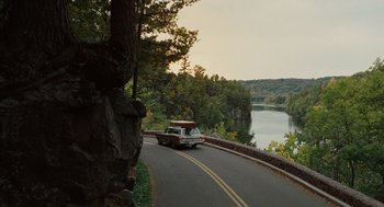 Movie still from “A Serious Man” (2009), directed by Joel Coen – A car driving down a road next to a body of water; Extreme Wide shot, High angle