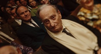 Movie still from “A Serious Man” (2009), directed by Joel Coen – An old man in a suit and tie with other people behind him; Close Up shot, High angle