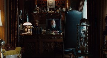 Movie still from “A Serious Man” (2009), directed by Joel Coen – An old man sitting at a desk in front of an old clock; Wide shot, High angle
