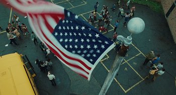 Movie still from “A Serious Man” (2009), directed by Joel Coen – An aerial view of a street with people walking around and an american flag on it; Extreme Wide shot, Overhead angle