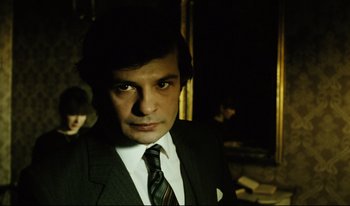 Movie still from “A Short Film About Killing” (1988), directed by Krzysztof Kieslowski – A man wearing a suit and tie in a dark room; Close Up shot, Over the shoulder angle