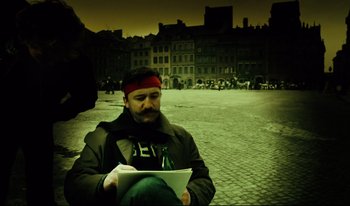 Movie still from “A Short Film About Killing” (1988), directed by Krzysztof Kieslowski – A man sitting on the ground holding a book; Medium shot, High angle