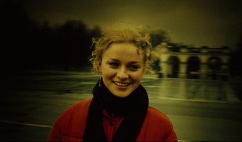 Movie still from “A Short Film About Killing” (1988), directed by Krzysztof Kieslowski – A young woman smiles for the camera in front of a bridge; Close Up shot, High angle