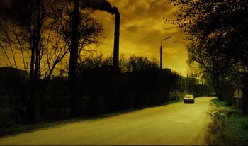 Movie still from “A Short Film About Killing” (1988), directed by Krzysztof Kieslowski – A car driving down a street near a factory with smoke coming out of the chimney; Extreme Wide shot, Low angle