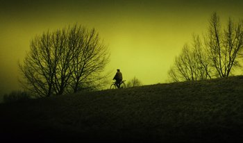 Movie still from “A Short Film About Killing” (1988), directed by Krzysztof Kieslowski – A man riding a bike on top of a grassy hill; Extreme Wide shot, Low angle