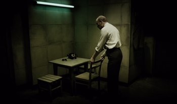 Movie still from “A Short Film About Killing” (1988), directed by Krzysztof Kieslowski – A man standing at a table in a dimly - lit room; Wide shot, High angle