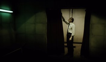 Movie still from “A Short Film About Killing” (1988), directed by Krzysztof Kieslowski – A man standing in front of an open door; Medium shot, Low angle