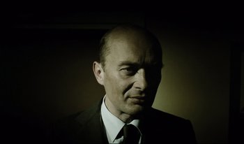 Movie still from “A Short Film About Killing” (1988), directed by Krzysztof Kieslowski – A man wearing a suit and tie in a dark room; Close Up shot, Low angle
