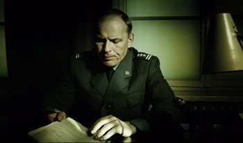 Movie still from “A Short Film About Killing” (1988), directed by Krzysztof Kieslowski – A man in a military uniform is reading a book; Medium shot, Low angle