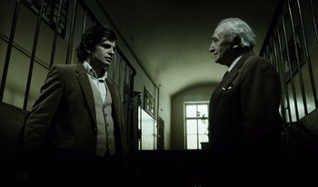 Movie still from “A Short Film About Killing” (1988), directed by Krzysztof Kieslowski – Two men in suits standing in front of a window; Medium shot, Low angle