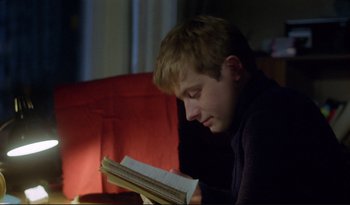 Movie still from “A Short Film About Love” (1988), directed by Krzysztof Kieslowski – A man sitting on a chair reading a book; Close Up shot, Over the shoulder angle