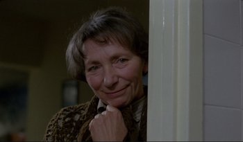 An older woman leaning against a white wall