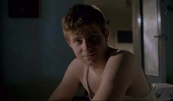 Movie still from “A Short Film About Love” (1988), directed by Krzysztof Kieslowski – A young man sitting in a room with his arms crossed; Close Up shot, Over the shoulder angle
