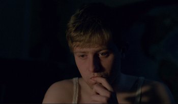 Movie still from “A Short Film About Love” (1988), directed by Krzysztof Kieslowski – A young man sitting in the dark with his hand under his chin; Close Up shot, High angle