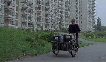 Movie still from “A Short Film About Love” (1988), directed by Krzysztof Kieslowski – A man pushing a cart full of boxes down a street; Wide shot, Low angle