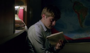 Movie still from “A Short Film About Love” (1988), directed by Krzysztof Kieslowski – A man sitting in front of a window holding a book; Medium shot, Low angle