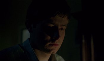 Movie still from “A Short Film About Love” (1988), directed by Krzysztof Kieslowski – A young man is looking at the camera with a dark background; Close Up shot, Low angle
