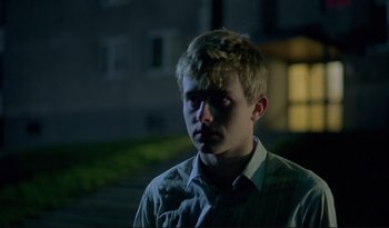 Movie still from “A Short Film About Love” (1988), directed by Krzysztof Kieslowski – A young man is looking at the camera while standing in the dark; Close Up shot, Low angle