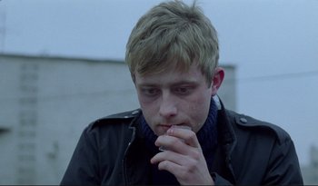 Movie still from “A Short Film About Love” (1988), directed by Krzysztof Kieslowski – A young man is smoking a cigarette while wearing a black jacket; Close Up shot, Over the shoulder angle