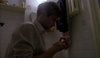 Movie still from “A Short Film About Love” (1988), directed by Krzysztof Kieslowski – A man in a white shirt is looking at his cell phone; Close Up shot, Low angle