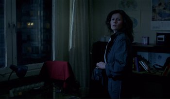 Movie still from “A Short Film About Love” (1988), directed by Krzysztof Kieslowski – A woman standing in front of a window in a dark room; Medium shot, Over the shoulder angle