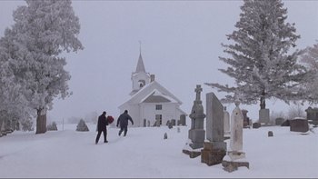 Movie still from “A Simple Plan” (1998), directed by Sam Raimi – Two people walking in the snow near a cemetery; Extreme Wide shot, Low angle