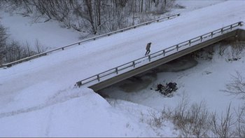Movie still from “A Simple Plan” (1998), directed by Sam Raimi – A man riding a skate board across a snow covered bridge; Extreme Wide shot, High angle