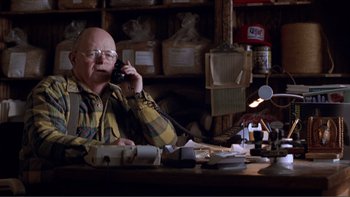 Movie still from “A Simple Plan” (1998), directed by Sam Raimi – An older man sitting at a table talking on a phone; Medium shot, Low angle